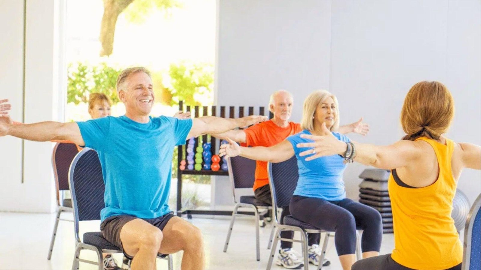 Group class doing seated arm stretches on chairs for a 28 day chair yoga challenge for seniors.