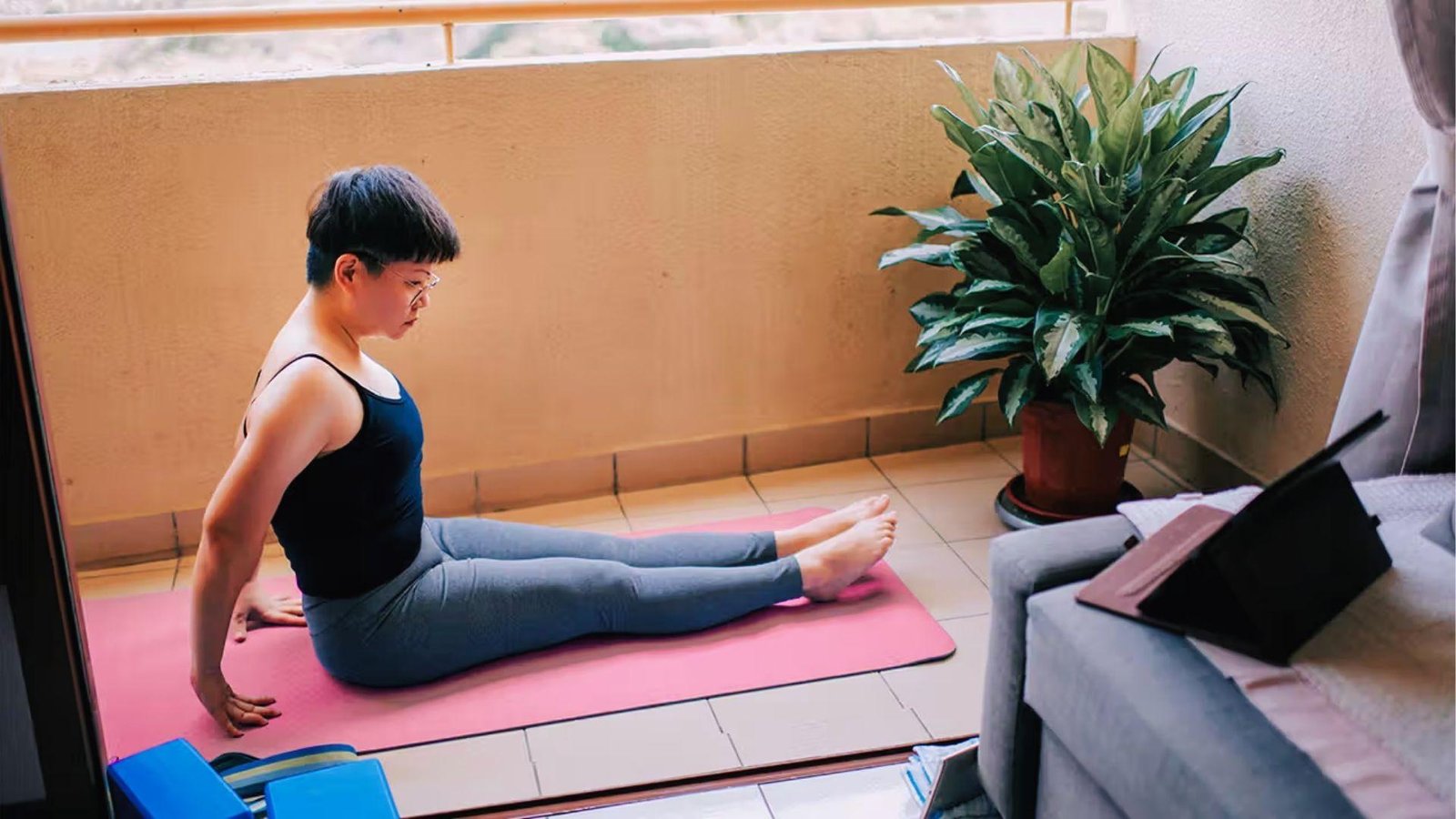 Person practicing staff pose on the balcony proves even beginner yoga movements activate core and burn calories.
