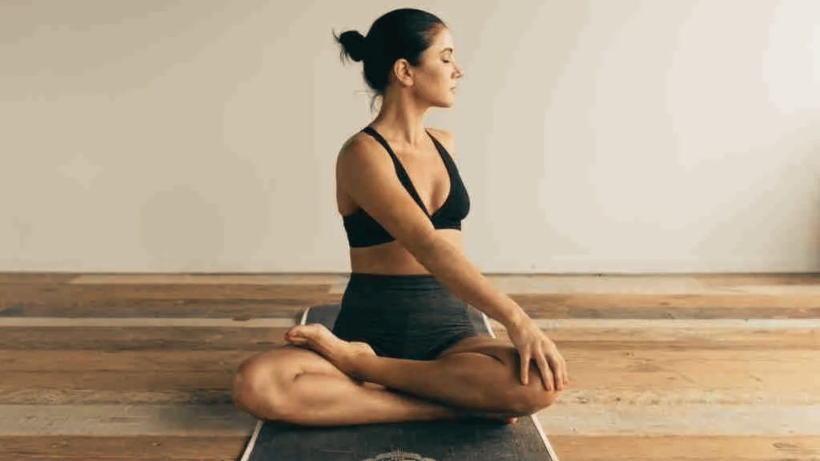 Woman sits cross-legged on a mat, gently twisting her torso with one hand on her knee.