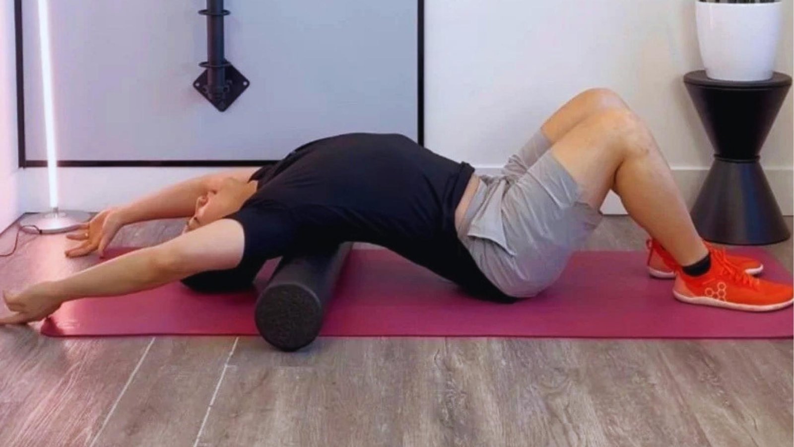Man lies on foam roller with arms overhead and knees bent, extending thoracic spine to improve mid-back mobility.