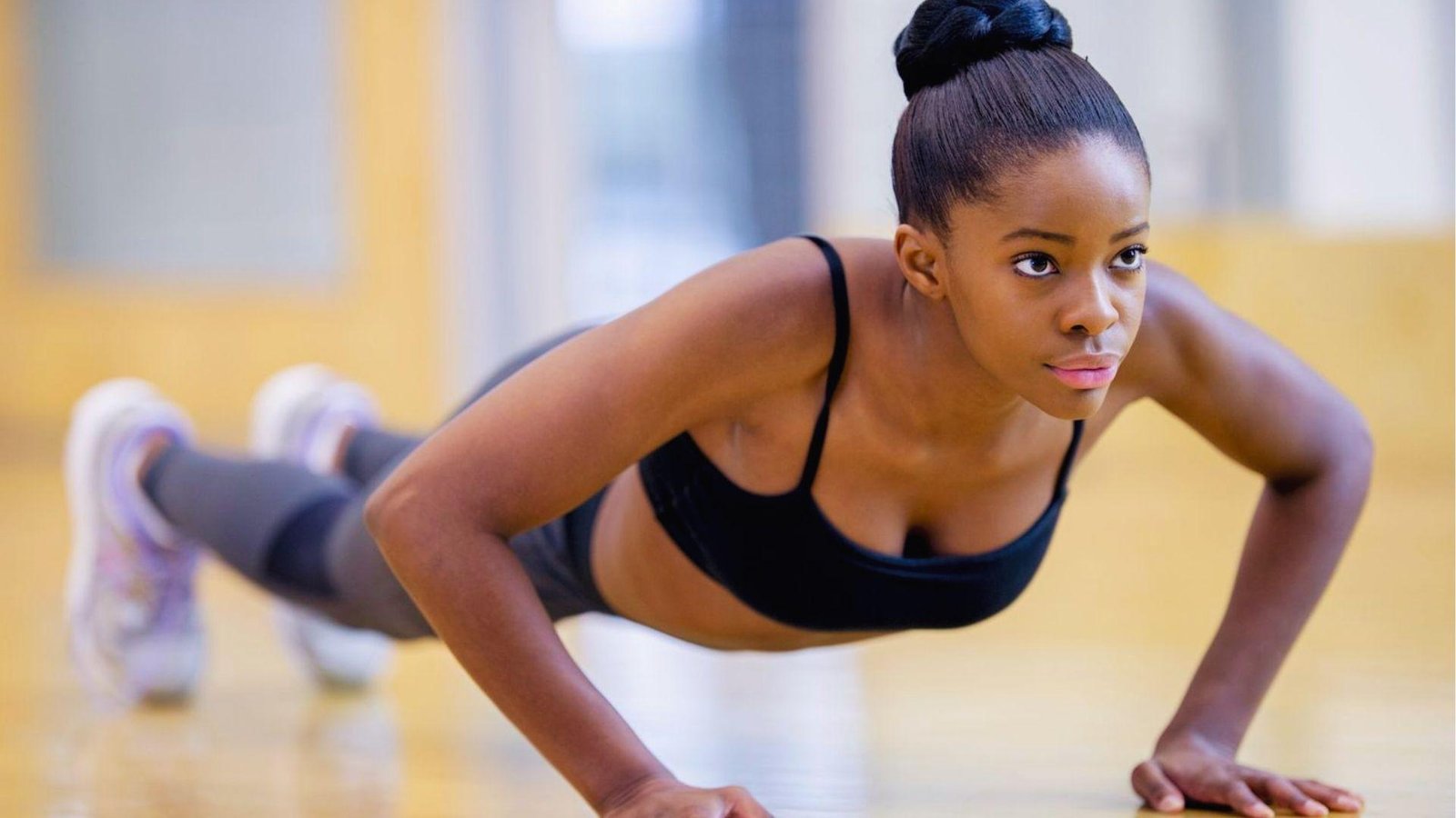 A focused woman holds a low Chaturanga yoga push-up with elbows tucked close to the gym floor.