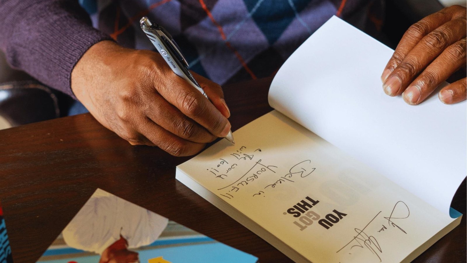 Close-up of hands writing "Believe in Yourself, You Got This" in journal, practicing affirmations for self-compassion.