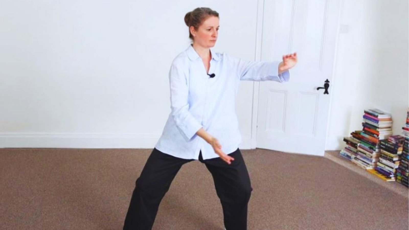 Woman in white shirt performs "Part the Wild Horse's Mane" Tai Chi move indoors, stepped stance, arms extended.