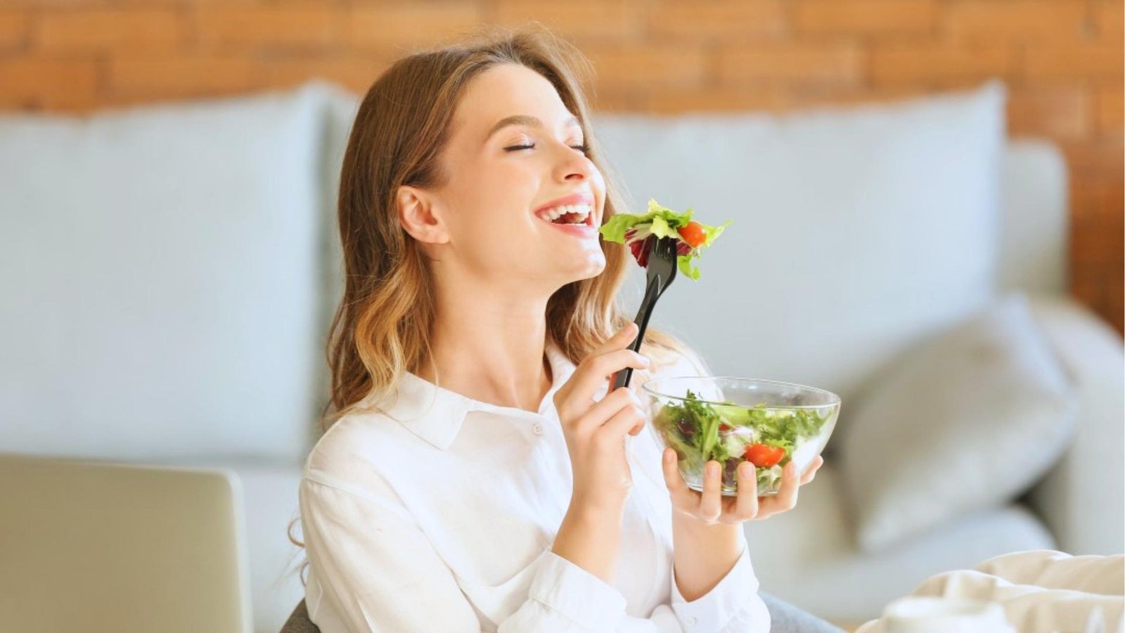 Woman in white shirt smiles while mindfully eating salad, chewing slowly to support digestion and vagal tone.