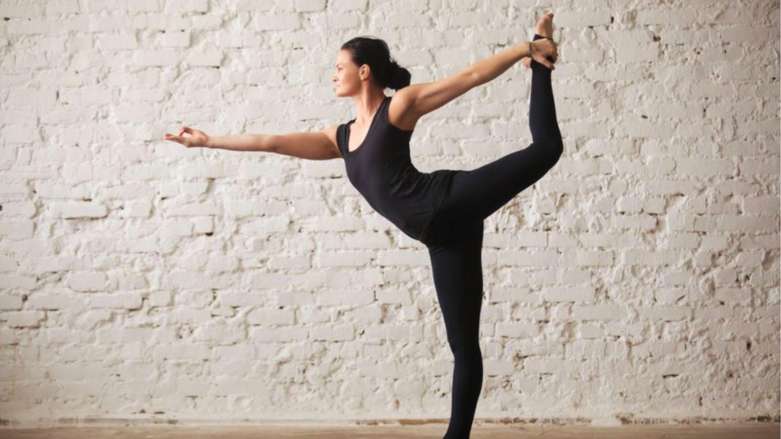 A woman in black activewear performing a dancer pose gracefully.