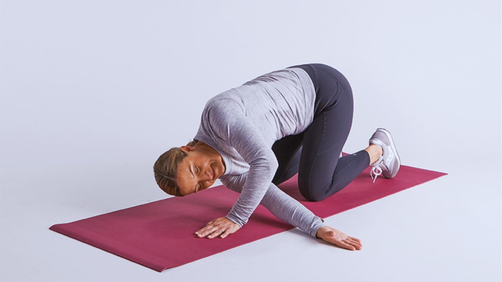 Woman in gray shirt does Thread the Needle pose on all fours, threading arm under body to rotate upper spine.