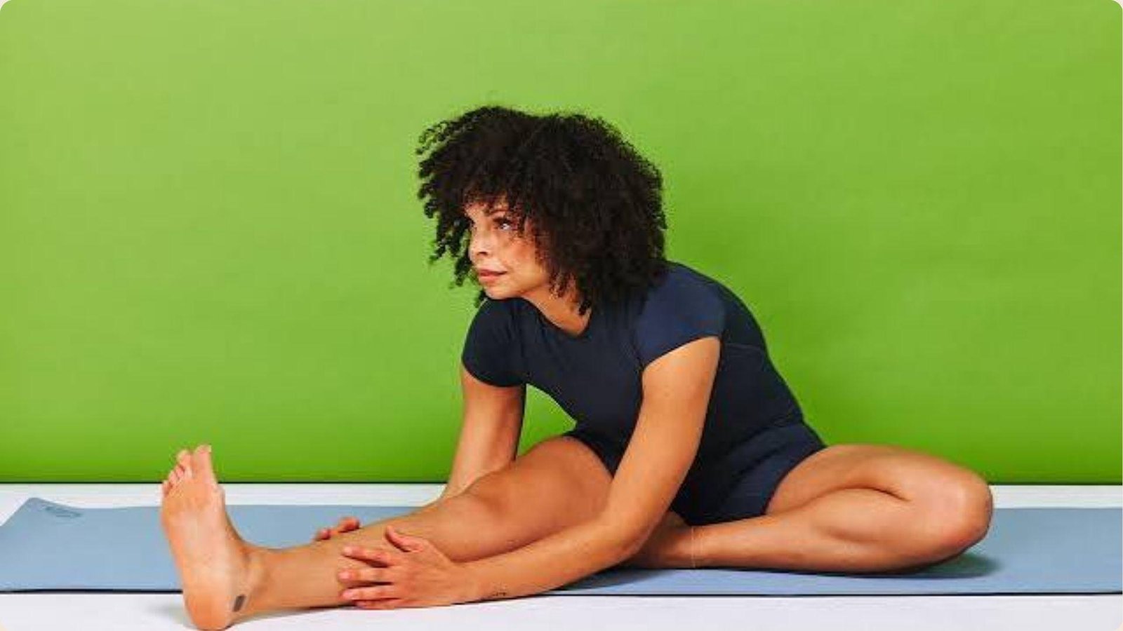 A woman sits cross-legged on a yoga mat, practicing mindfulness in a serene indoor environment.