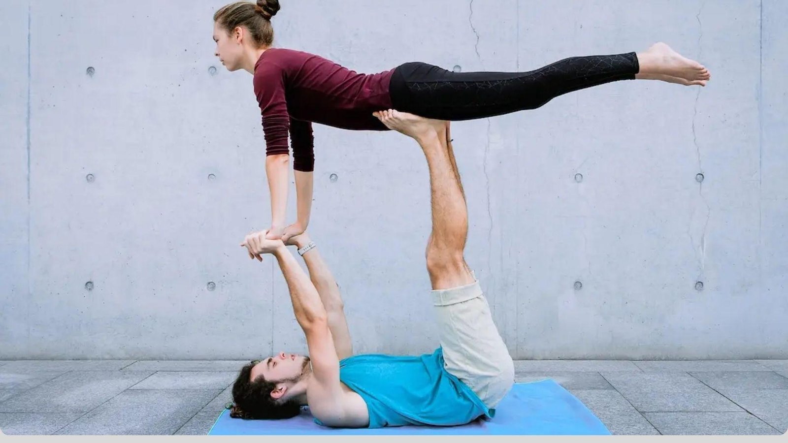 Two people practicing beginner acro yoga poses on a soft mat, focusing on trust, balance, and partner coordination in a studio setting.
