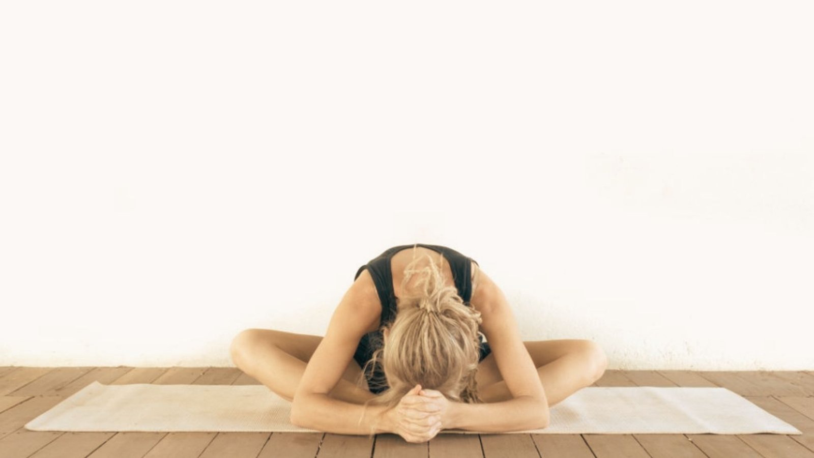 Woman seated on a yoga mat in yin yoga Butterfly pose, folding forward with soles of feet together and head lowered toward the floor.