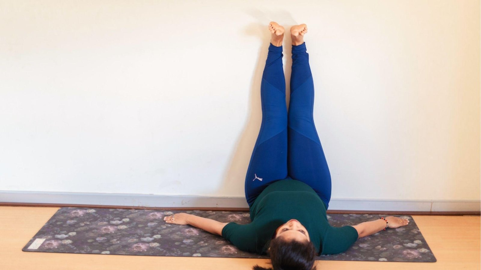 Woman lying on mat in wall yoga legs-up-the-wall pose to relax and improve circulation.