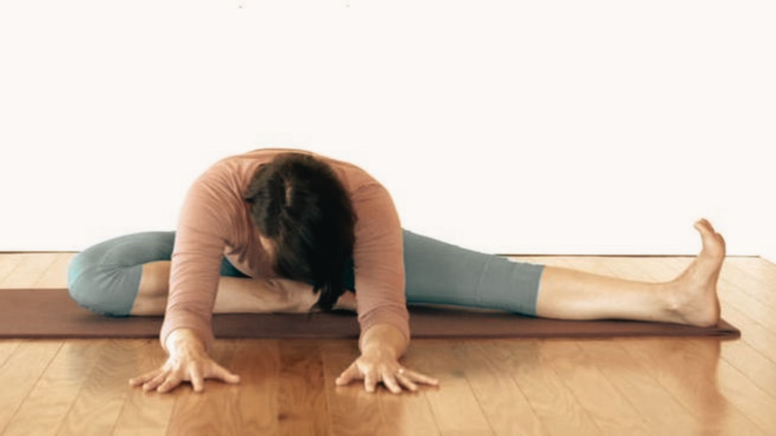 Woman in yin yoga Half Butterfly pose, folding forward over an extended leg while the other foot rests against the inner thigh.
