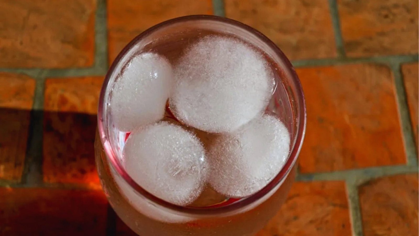 Top-down view of glass with ice water on brick tiles, cold exposure technique used for vagus nerve activation.