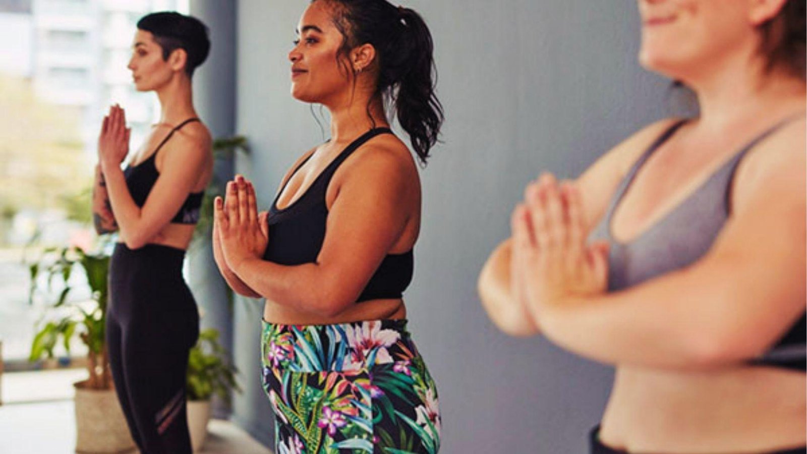 Three women in prayer pose at a studio class showing gentle yoga can still engage muscles and burn calories.