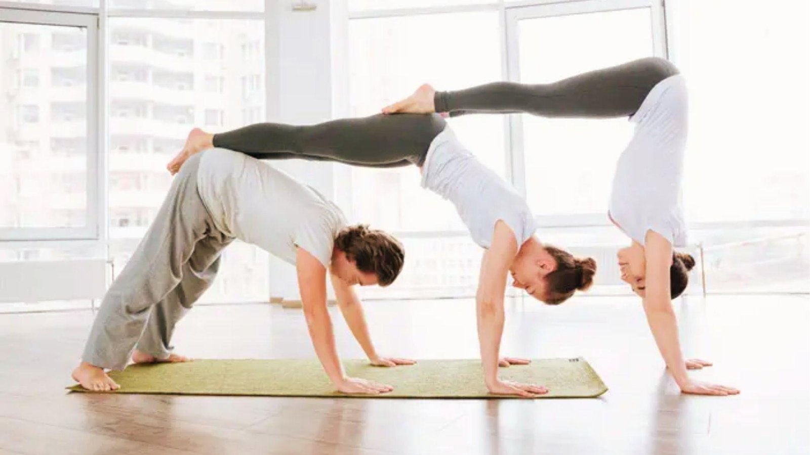 Three people create a 3 person yoga stack with downward dog base and handstand top.