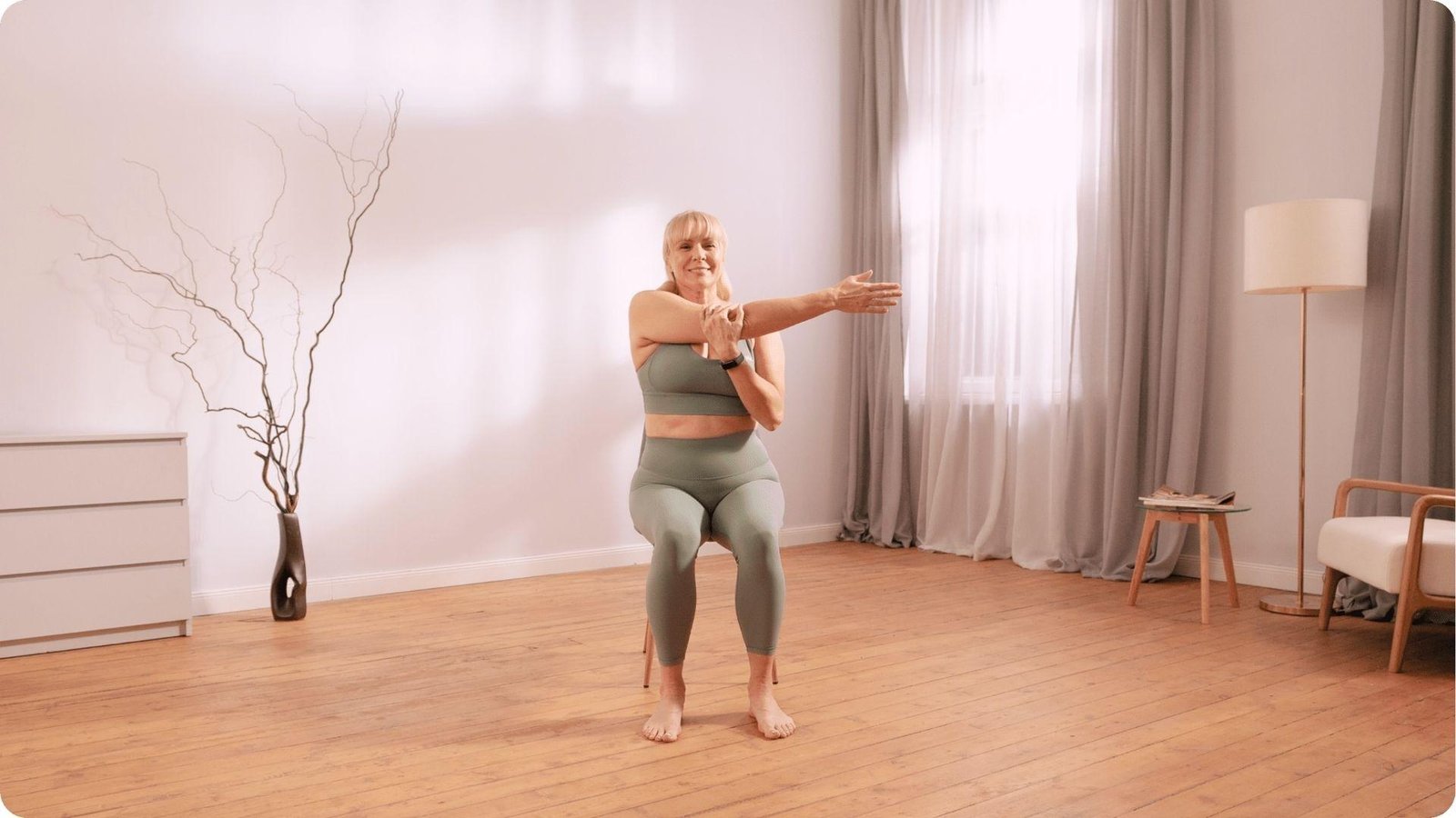 Woman in sage outfit doing seated shoulder stretch for 28 day chair yoga challenge flexibility.
