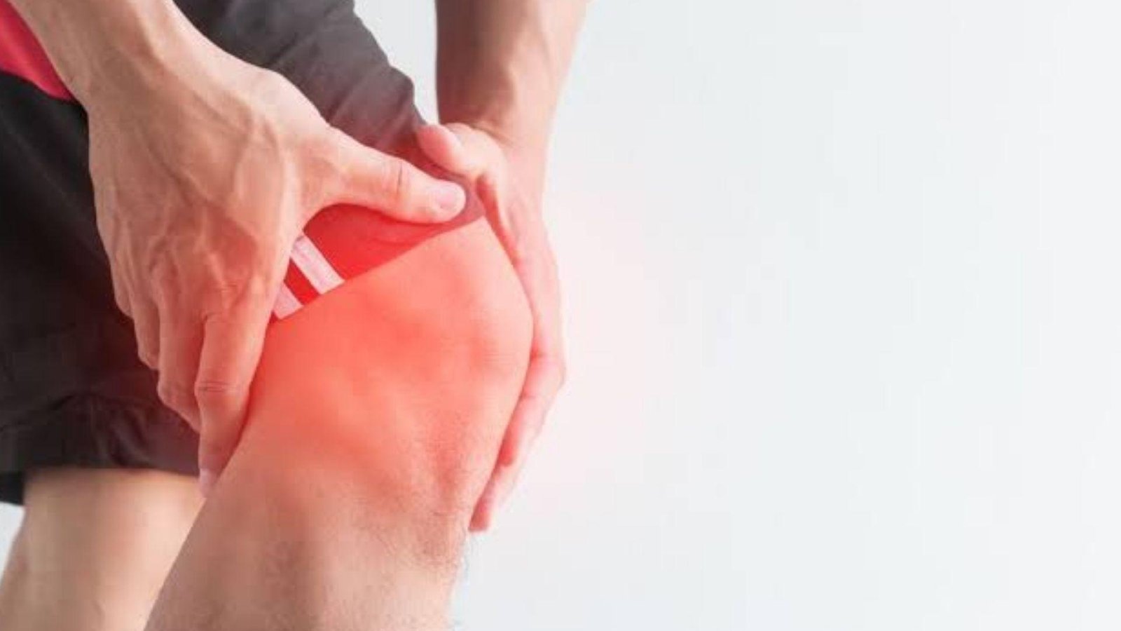 A man grimaces while holding his knee, indicating discomfort from knee pain.
