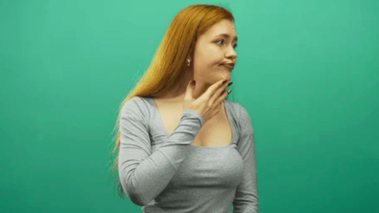 Woman in gray top touching her throat while pursing lips to the side.