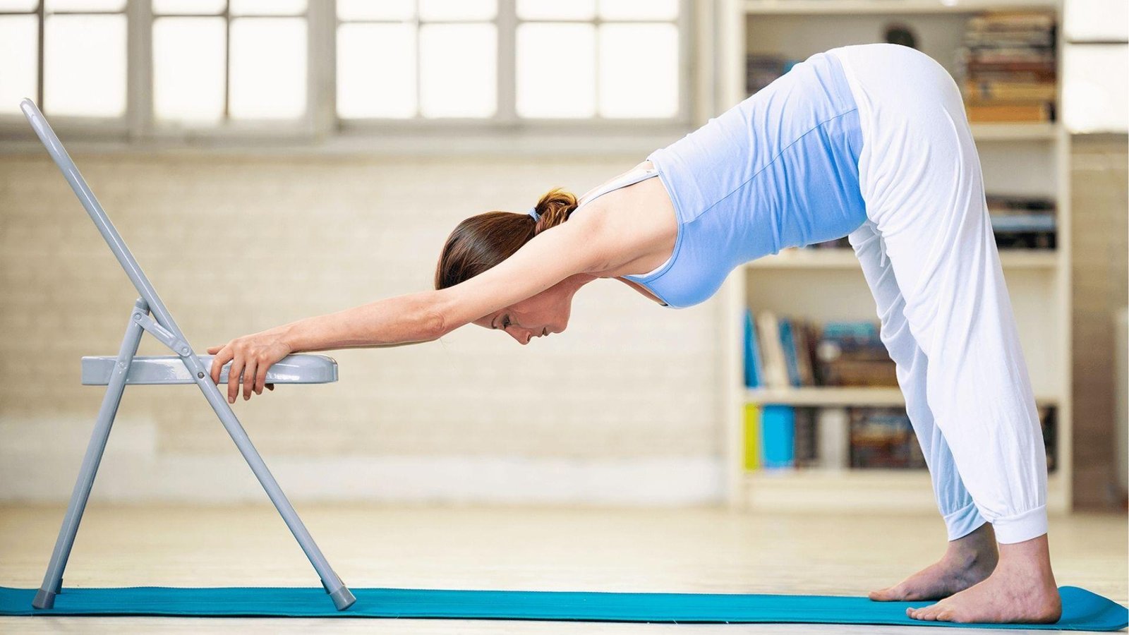 Woman doing chair downward dog stretch on yoga mat for 28 day chair yoga challenge at home.