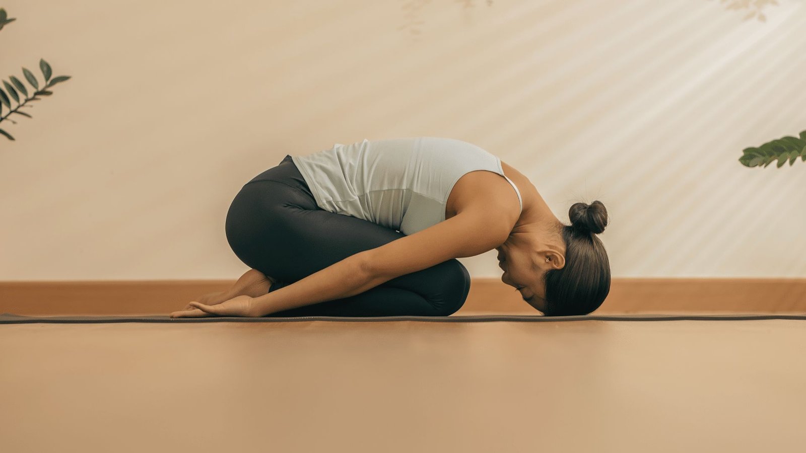 Woman in Child’s Pose on a yoga mat, forehead resting down with arms extended back in a calming space.
