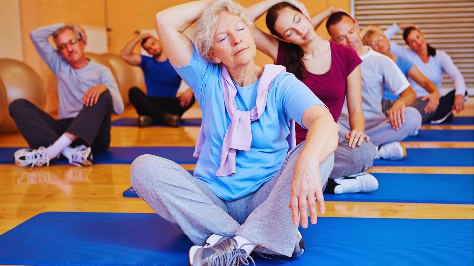 Senior woman in blue shirt performs gentle seated neck stretch in group yoga class to stimulate vagus nerve.