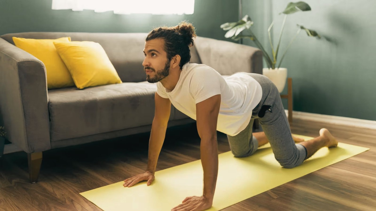Man practices a low lunge on a yellow mat in a living room, gazing forward with steady breath.