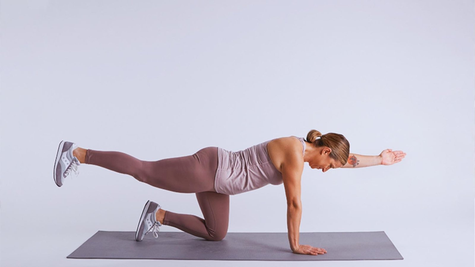 Woman in mauve workout set does Bird Dog on mat, extending opposite arm and leg for core stability.