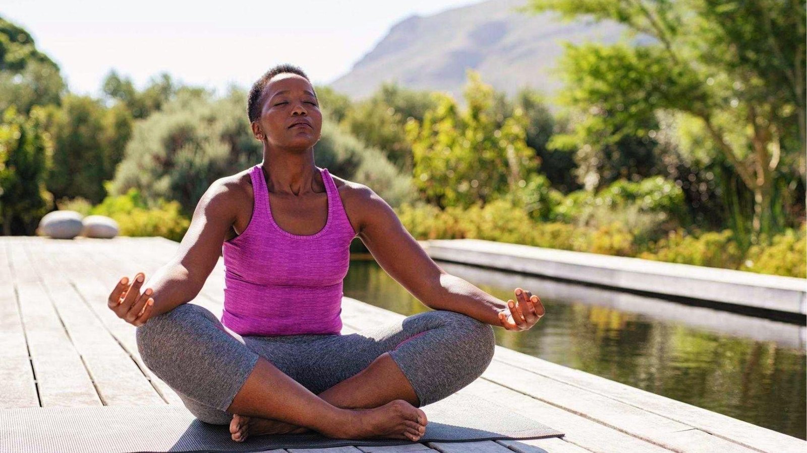 Woman meditating in lotus pose by water shows restorative yoga burns fewer calories but aids recovery.