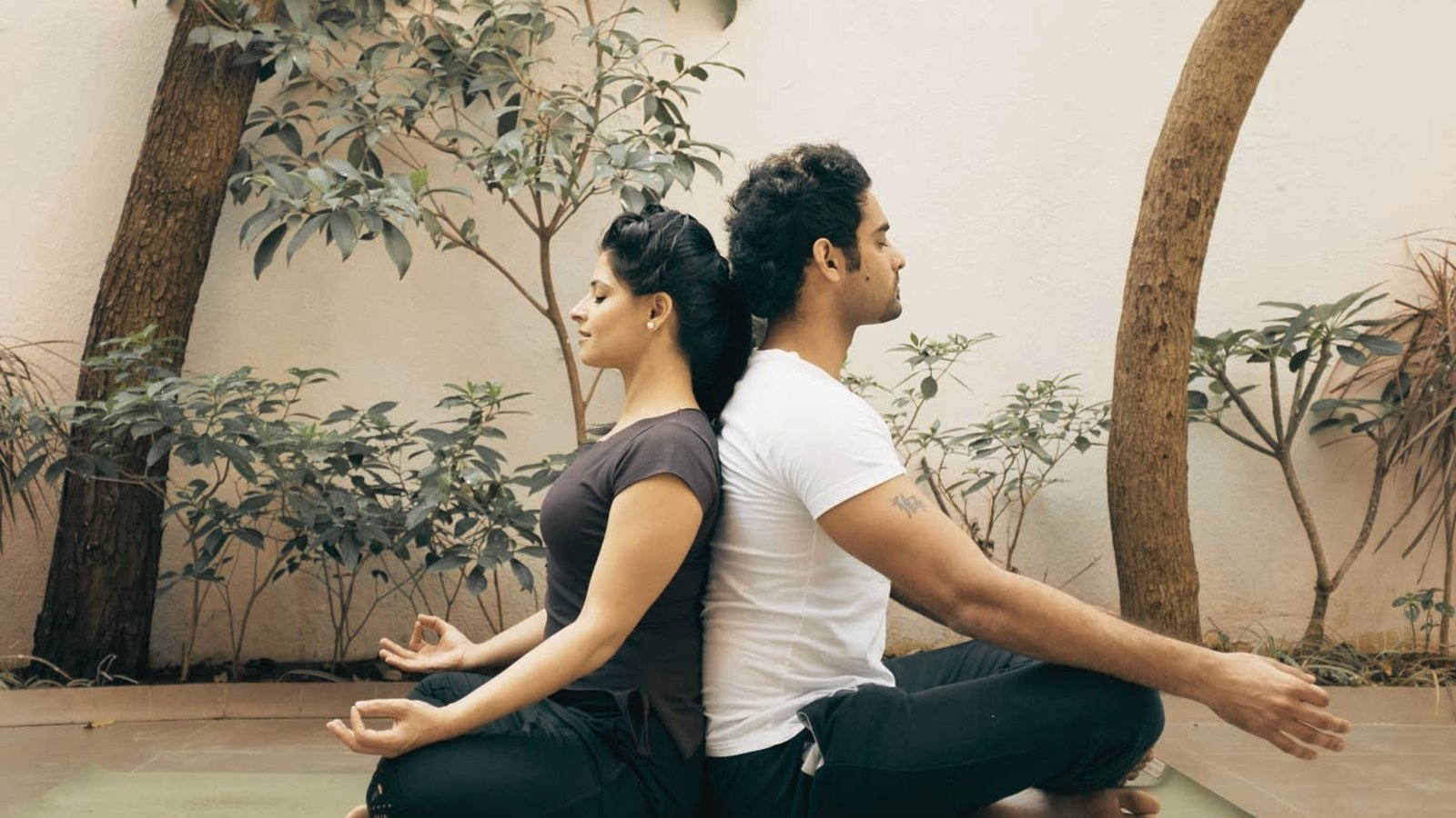 Two women practice partner yoga in a bright studio with other students in the background.