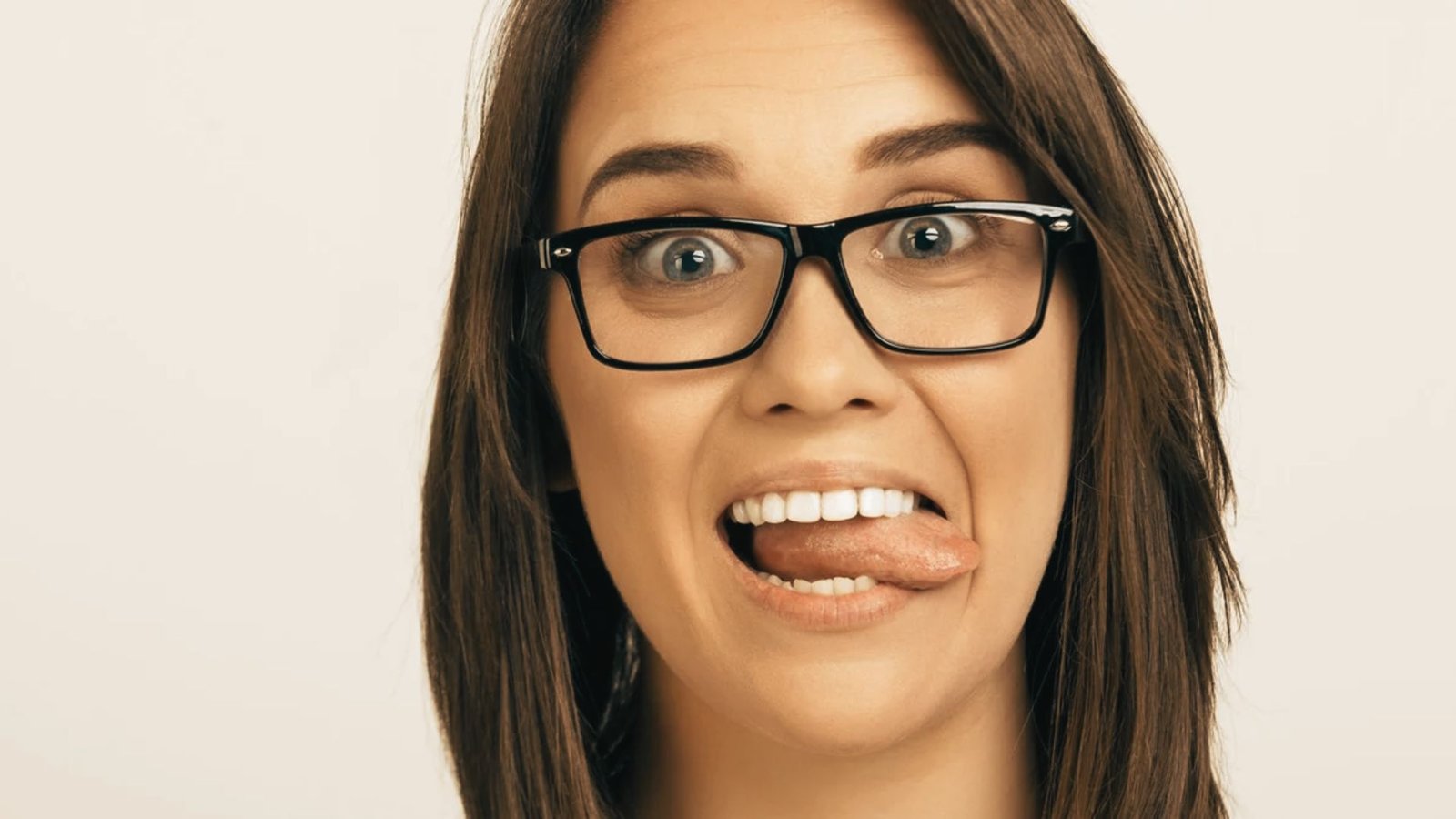 Woman wearing glasses performs a tongue-to-lower-teeth exercise by pushing her tongue against her bottom front teeth.