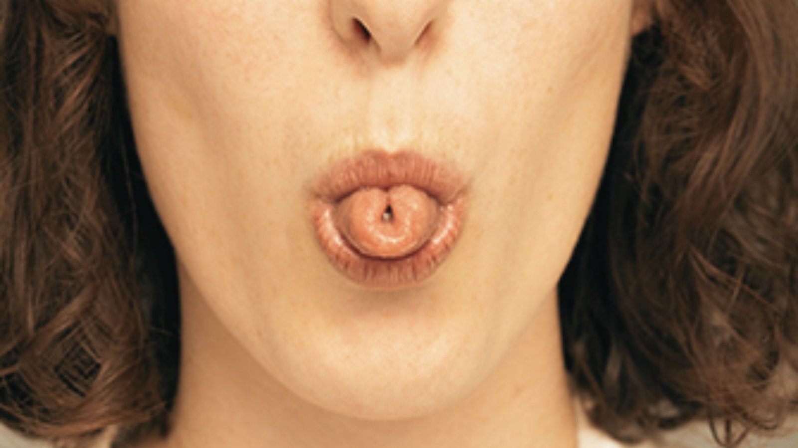 Person with curly hair forming a tongue roll inside pursed lips.