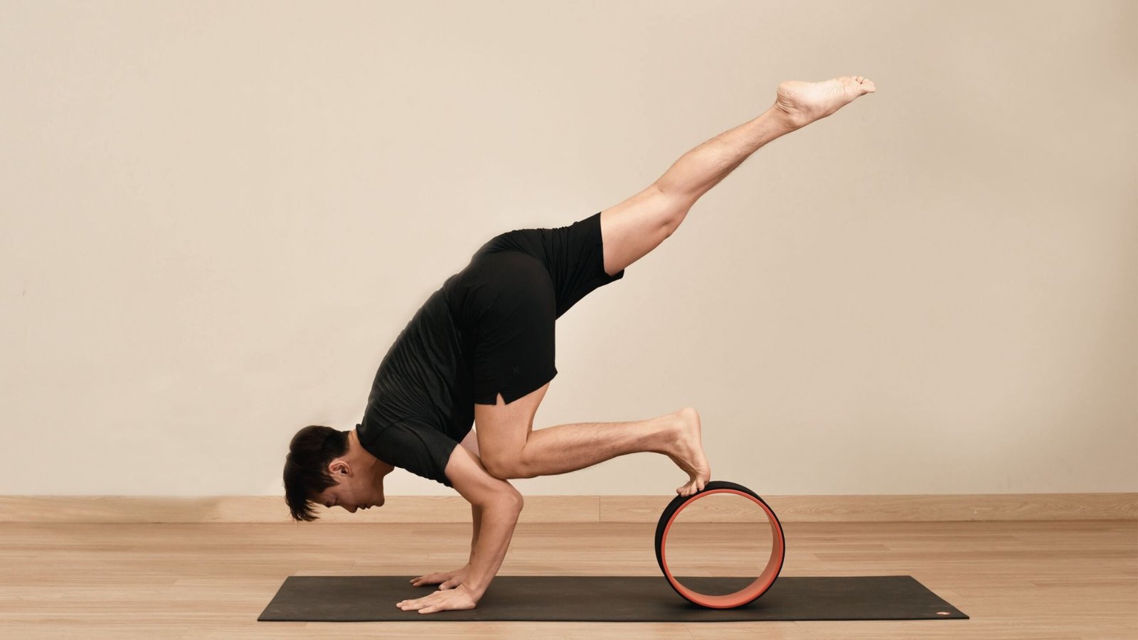 Person balances on hands with one foot on a yoga wheel and one leg raised.
